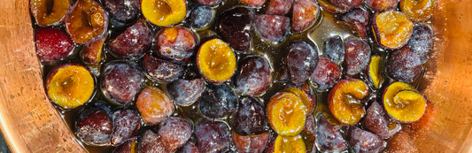 Halved plums macerating in copper pan for plum and star anise jam